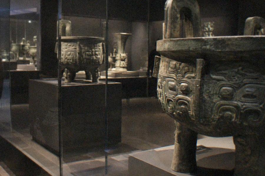 Ancient Chinese bronze vessels lit in glass display cases inside a museum gallery