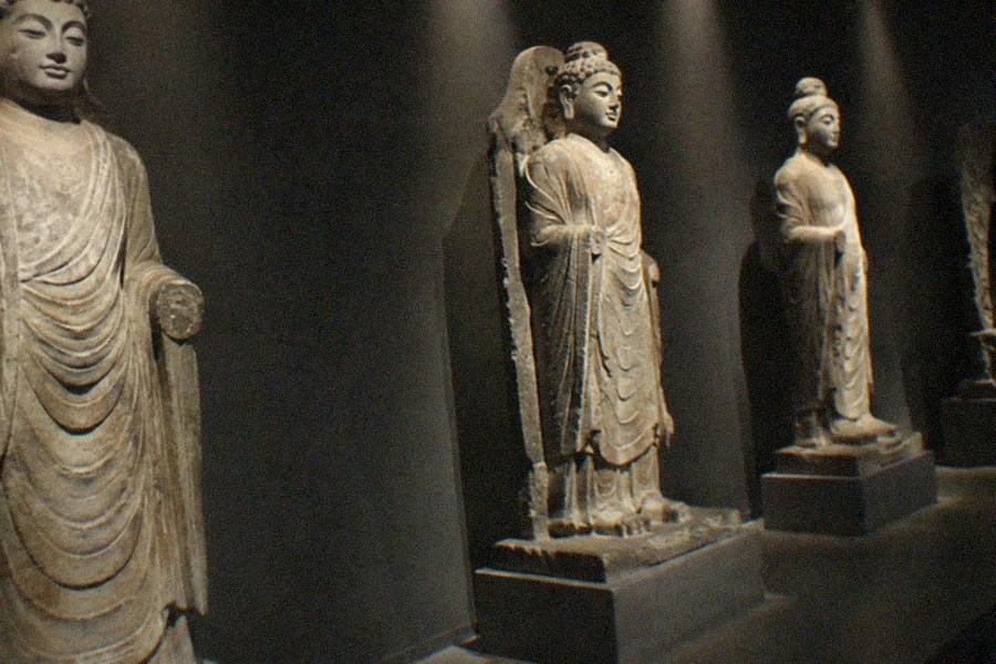 A museum gallery hall with bronze sculptures in spotlit vitrines and dark stone walls